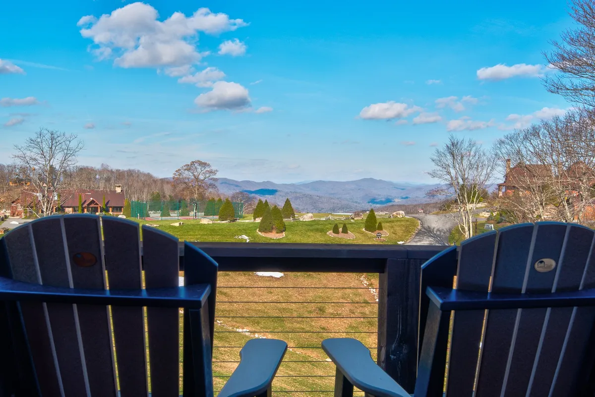 A pair of Adirondack chairs are positioned to face a breathtaking mountain view under a clear blue sky. The setting is serene and designed for peaceful relaxation, with an emphasis on enjoying sunrise vistas and starry nights.