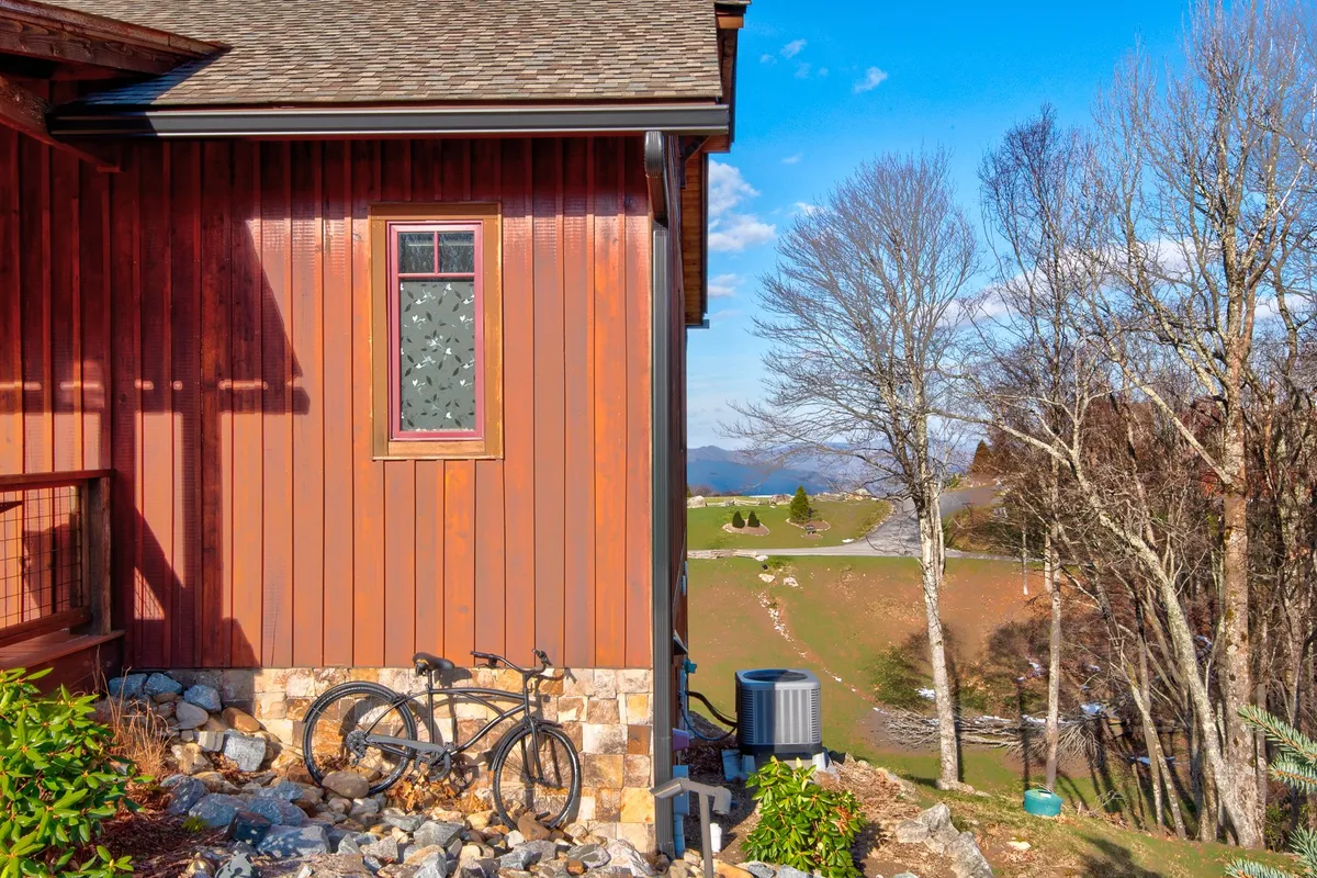 This exterior image features a charming cabin façade with wooden siding, a decorative window, a bicycle leaning against the stone foundation, and subtle landscaping touches. The setting exudes a relaxed, mountain-town vibe, hinting at outdoor adventure and the beauty of the surrounding area.