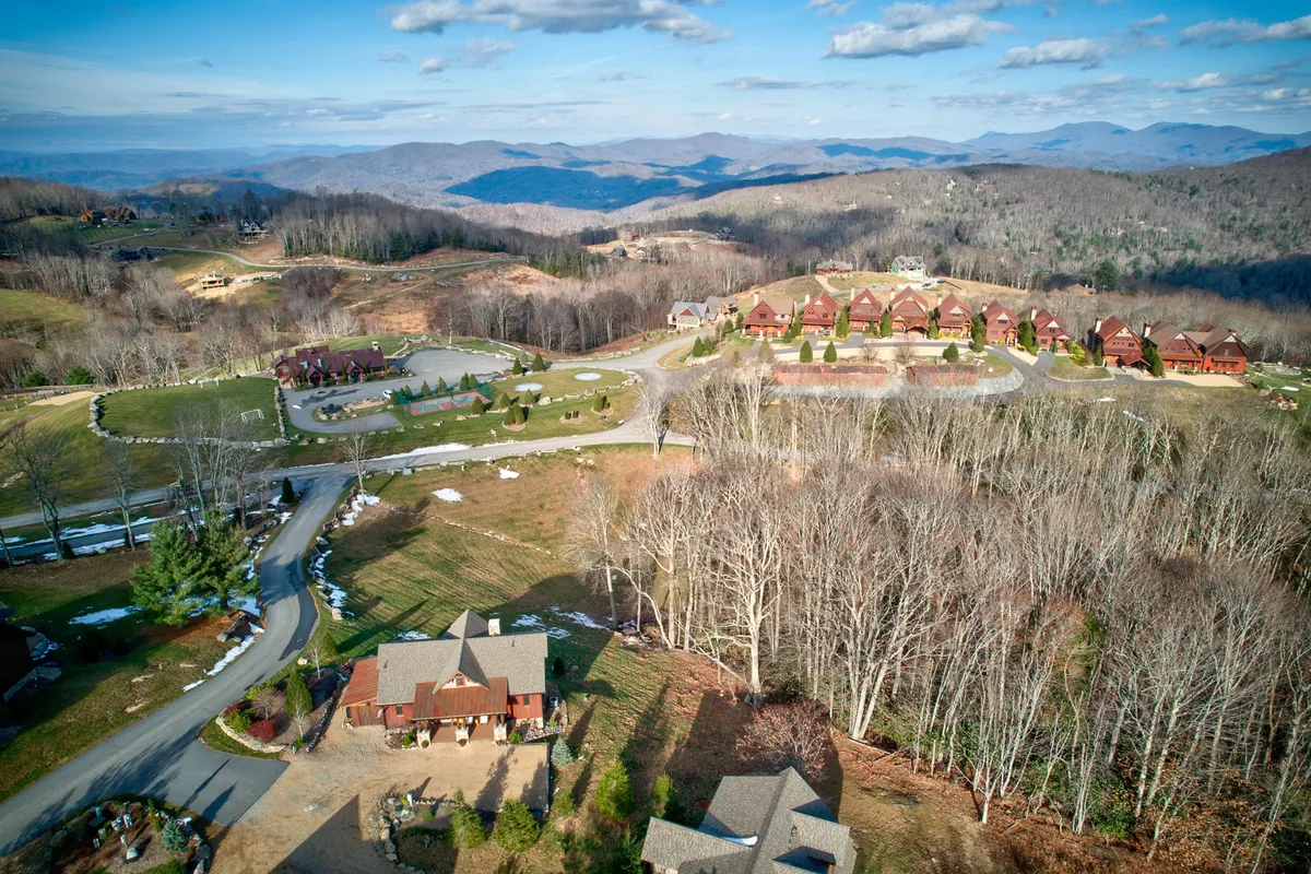 A panoramic view encompassing a sweeping mountain range with residential buildings nestled among winding roads and expansive open fields. The scene is tranquil, evoking a sense of adventure and connection to nature, while also capturing the spirit of a community setting.
