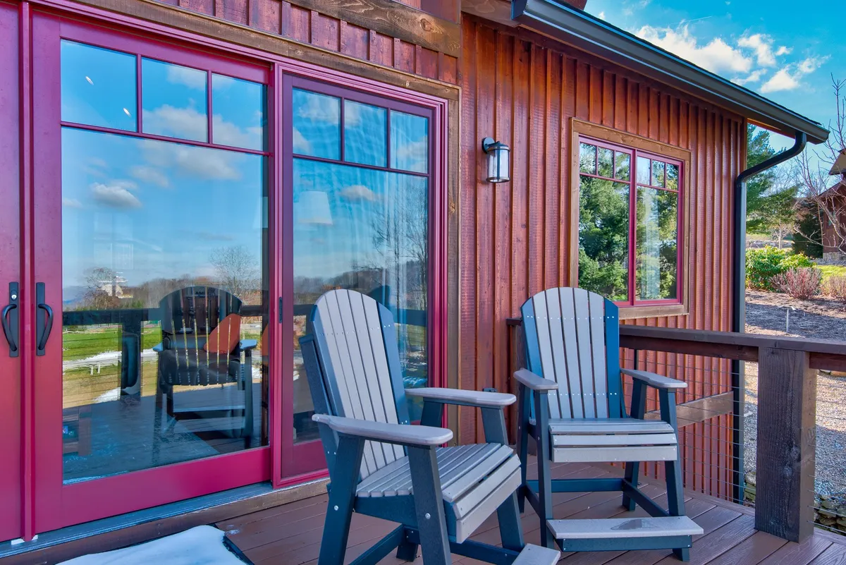 This cozy exterior scene presents rocking chairs on a wide, easily accessible porch with double doors and wooden siding. The atmosphere is calm, inviting, and perfect for socializing, relaxing, or simply enjoying the surrounding nature.