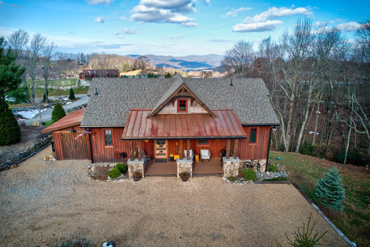 A rustic wooden facade with a metal roof and inviting front porch seating, surrounded by natural landscape. The scene feels welcoming and vibrant, ideal for relaxation, social gatherings, and observing seasonal festivities.