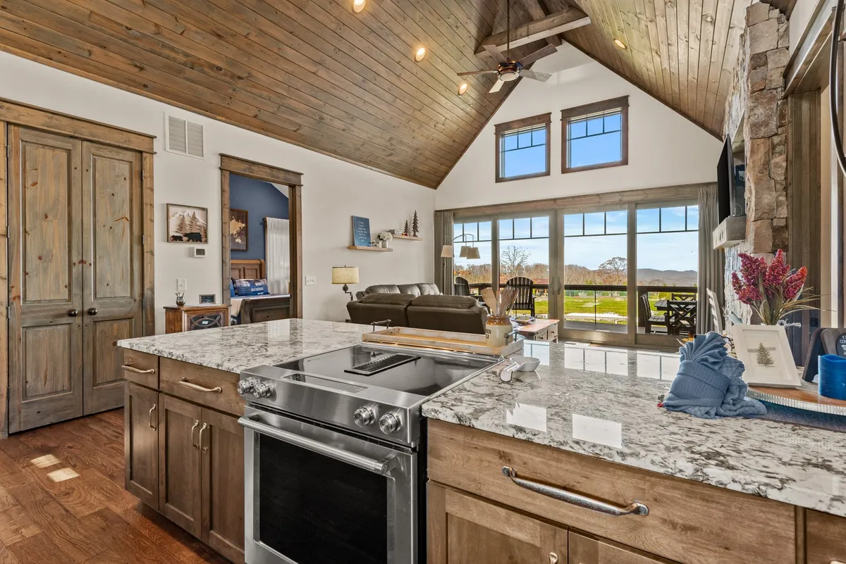 A beautiful interior view featuring a granite kitchen island, comfortable seating area, and large windows overlooking a breathtaking mountain landscape. The wooden ceiling with exposed beams adds warmth, and the setup encourages both relaxation and socialization.