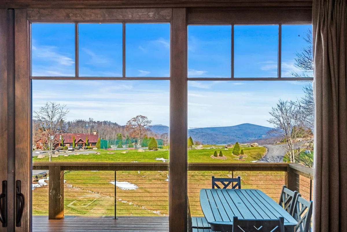 A wide view from a wooden deck, featuring an outdoor dining table perfectly positioned to enjoy sweeping mountain vistas. The scene is peaceful and inviting, with the deck acting as a private perch to take in sunrises or sunsets. The lush greenery and mountains in the distance highlight the natural beauty of the area.