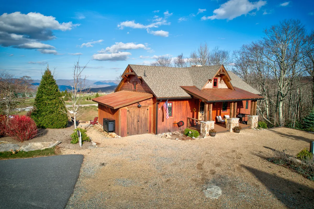 This tranquil exterior scene shows the rustic wooden façade with a landscaped garden and sweeping mountain views beyond. The porch is set up for morning coffee, stargazing, and gatherings, reinforcing the property's connection to the natural beauty of the Blue Ridge Mountains.