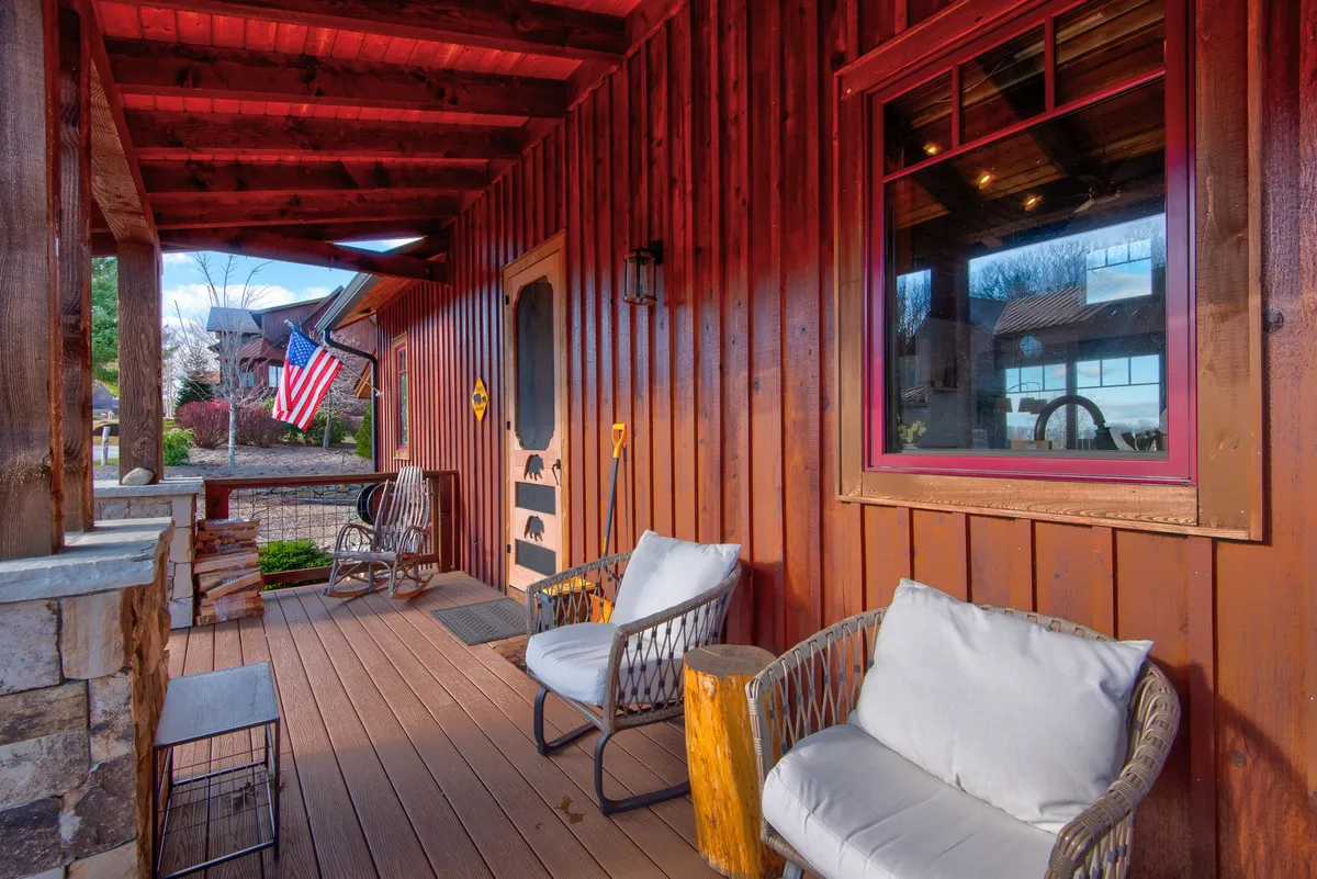 An inviting front porch scene with wooden chairs set beside a stone wall and the front door, adorned with an American flag. This area is designed for socializing, enjoying sunsets, and hosting barbecues, embodying the spirit of togetherness and outdoor enjoyment in all seasons.